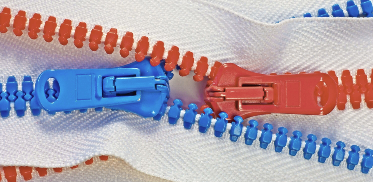Close-up photograph of a zipper with two differently coloured sides - one is bright red and the other is bright blue or turqouise. They meet in the middle.
