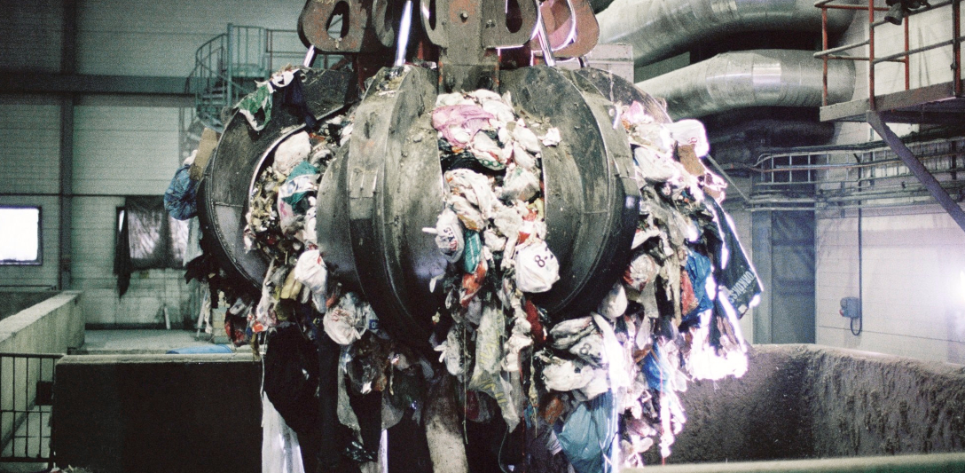 Image of a grapple grabbing a big piece of waste from a container in a waste incineration facility.