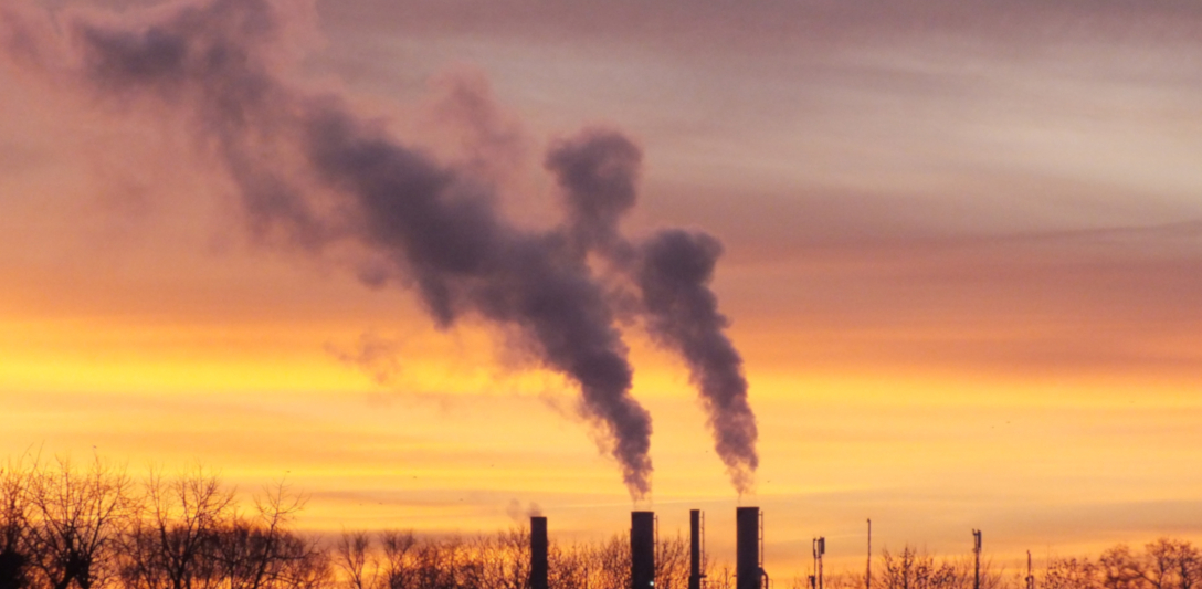 The image shows a smoking heating plant on a winter morning with a bright orange sunrise.