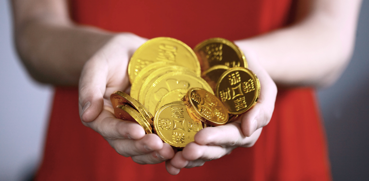 Person in a bright red dress holding out their hands in front of them and holding a small pile of golden coins.
